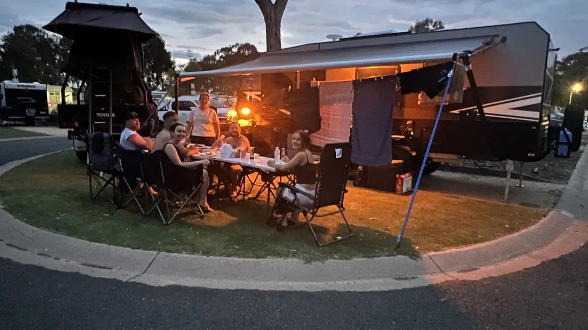 Family and friends sharing dinner under the caravan awning at dusk